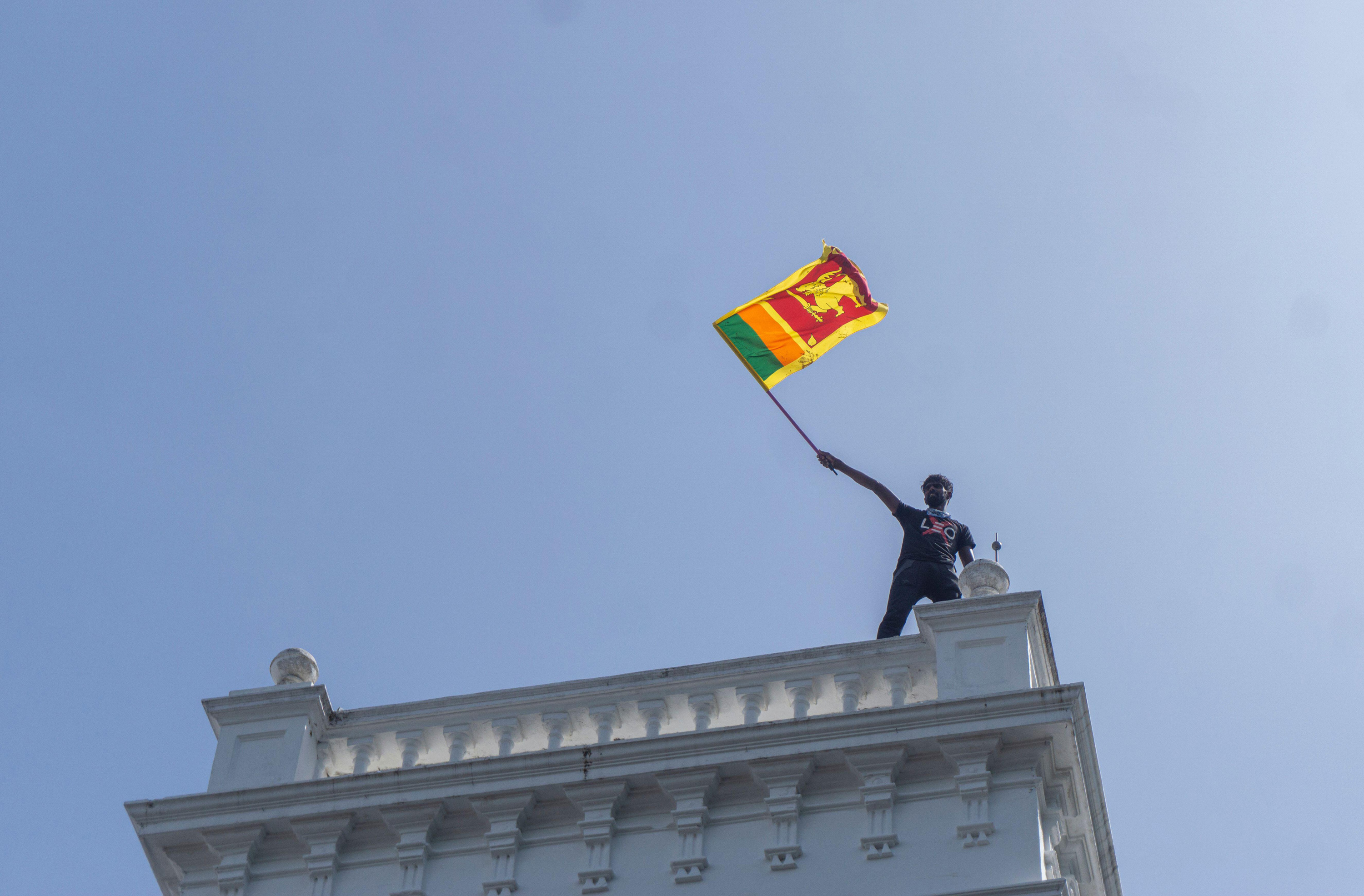 A protester waves a Sri Lankan flag while standing atop prime minister Ranil Wickremesinghe's office in Colombo on July 13, 2022. Hundreds of protesters stormed the office amid the deep political and economic crisis in the country which led to months of widespread protests.