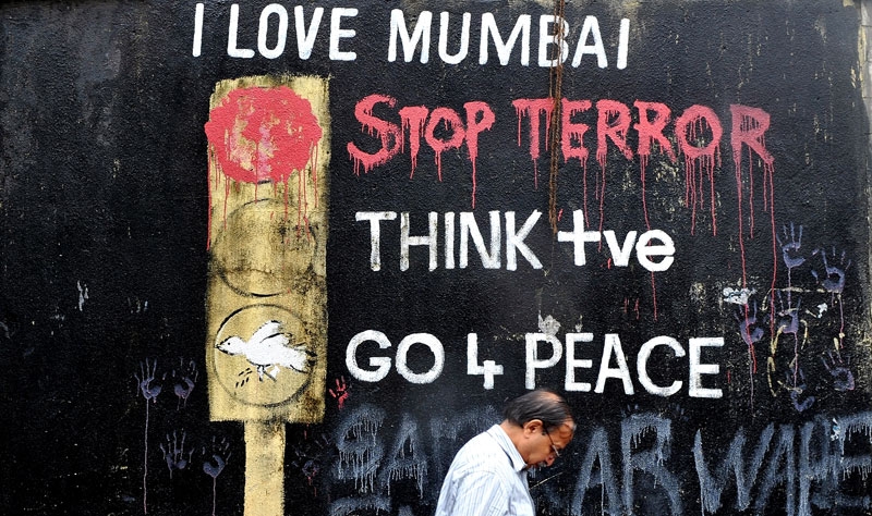 An Indian office worker walks past wall graffiti made after the 2008 terror attacks near the recent blast site at Opera House in Mumbai on July 14, 2011. (Indranil Mukherjee/AFP/Getty Images)