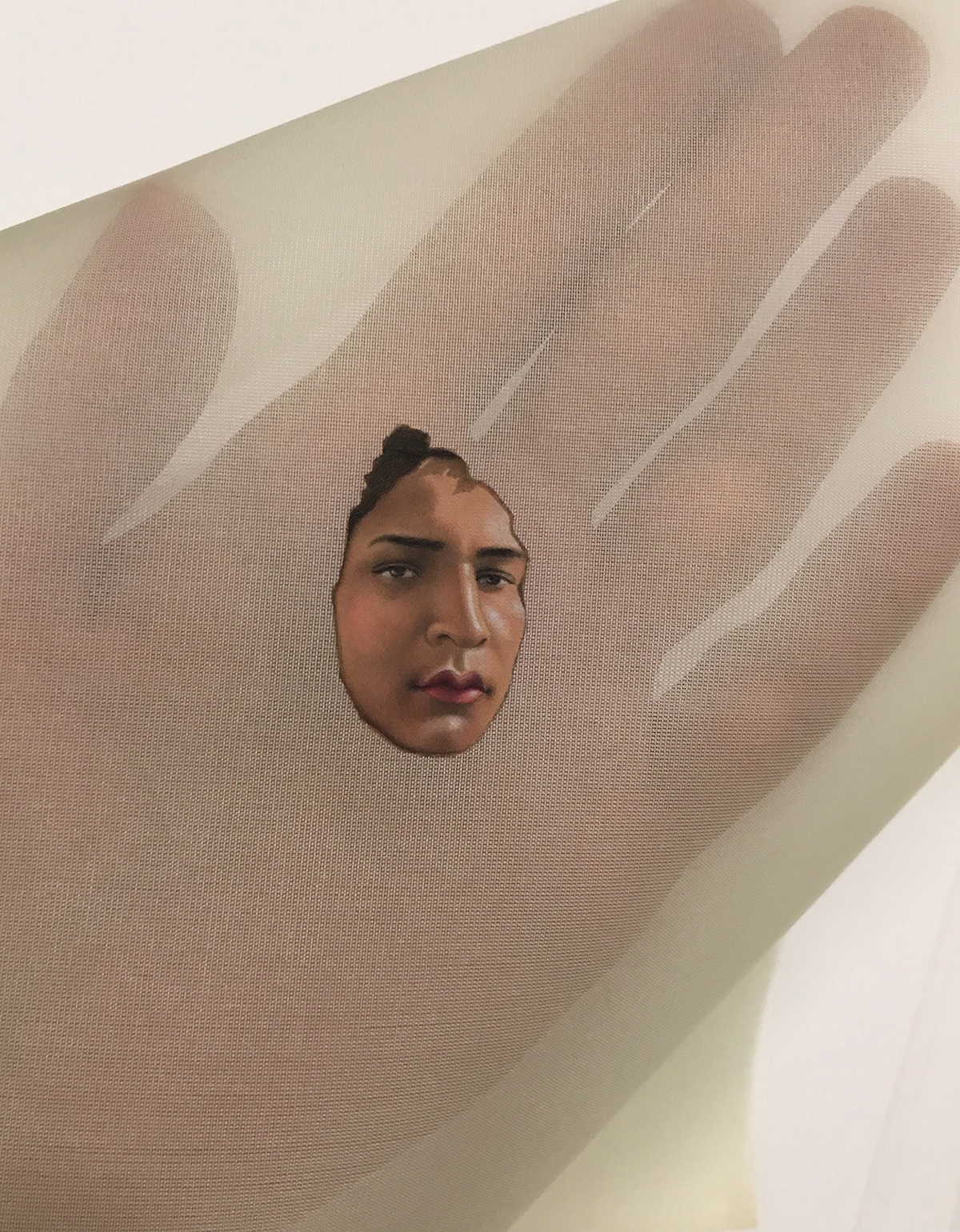 A hand is covered in a gauzy fabric. In the palm of the hand is a small image of a person's face