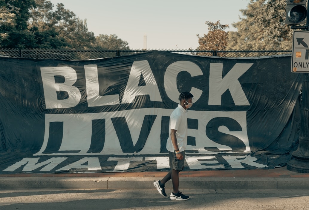Man walks in front of a Black Lives Matter flag