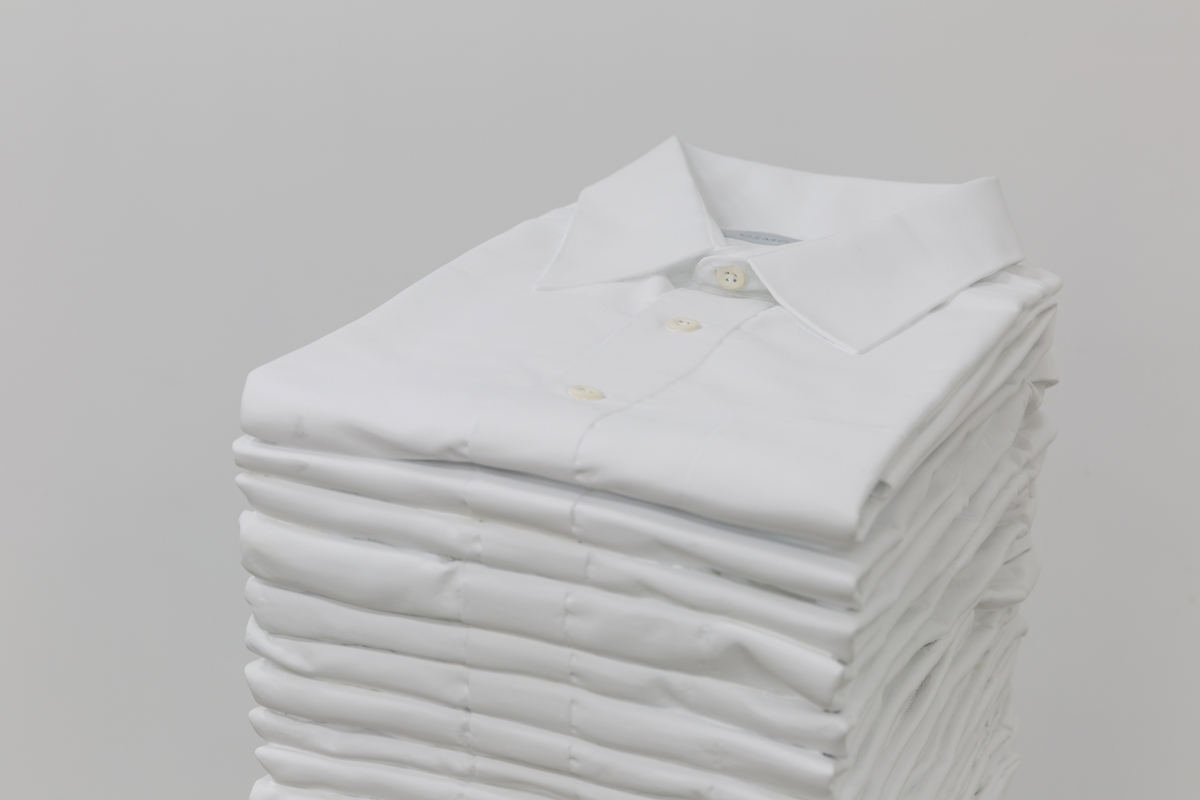 A stack of folded white collared shirts in front of a white background