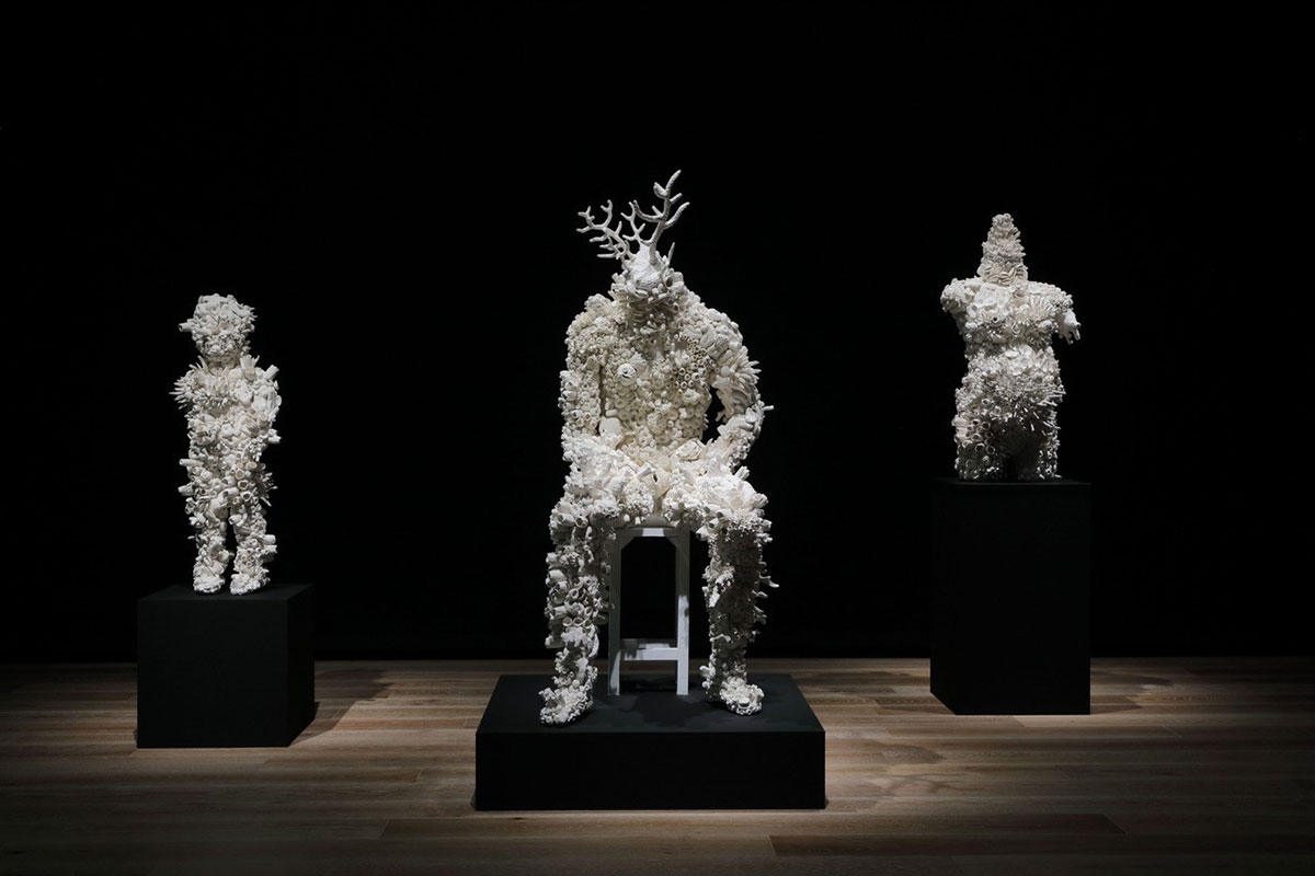 Three figurative sculptures appear on individual black plinths. Each is sculpture is composed of creamy white biomorphic forms that resemble coral.