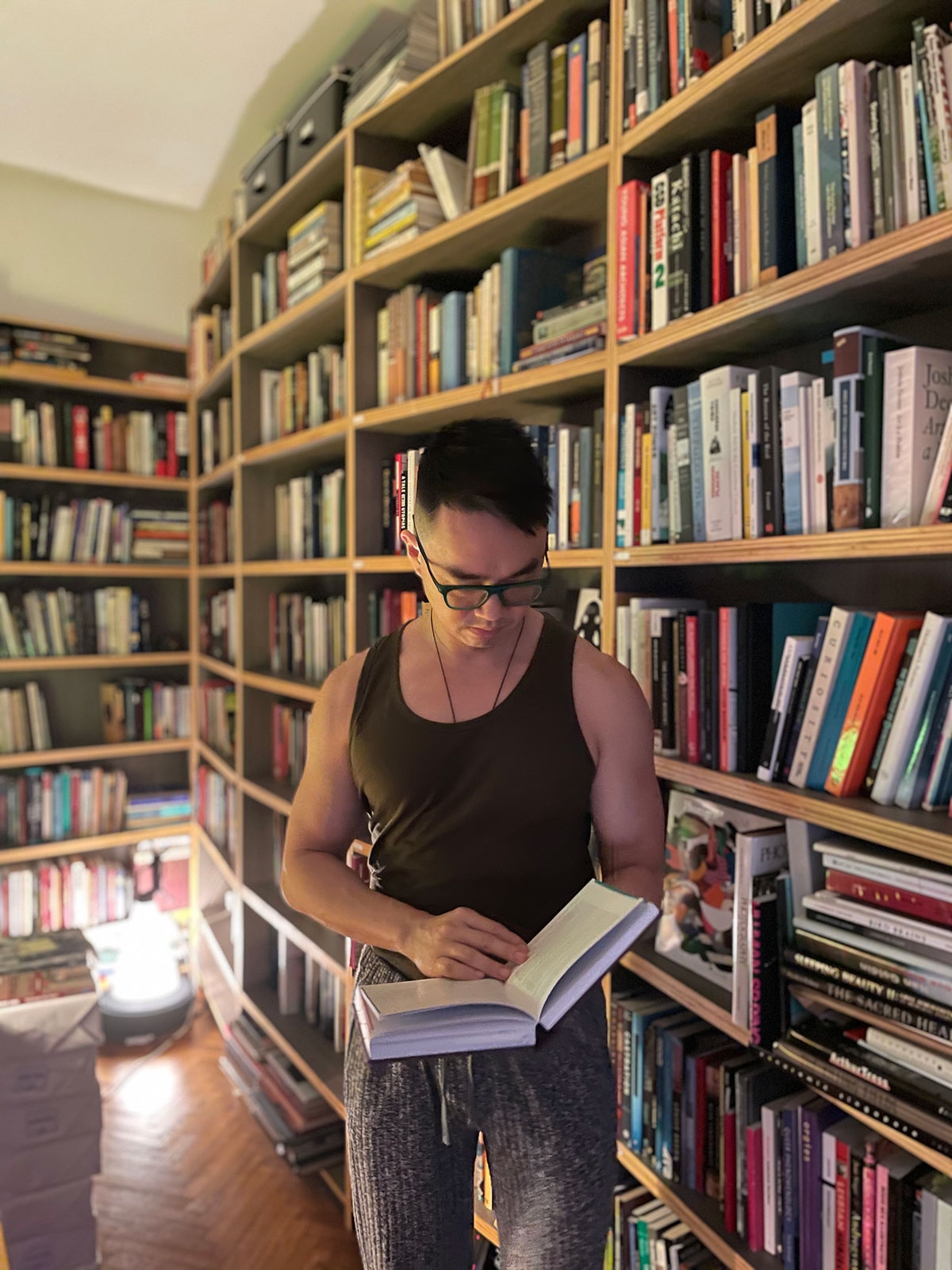 The artist stands in front of many bookcases, holding an open book. 