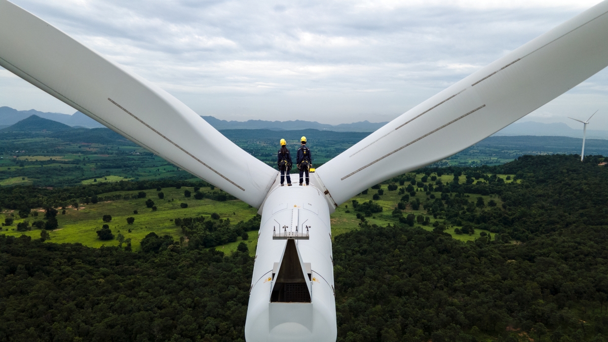 Two Electric engineer wearing Personal protective equipment working on top of wind turbine farm