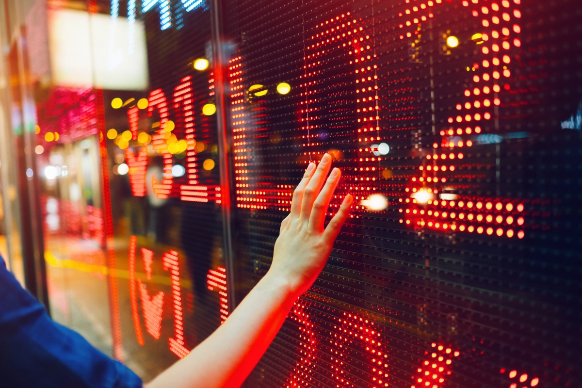 Woman's hand on stock exchange market display screen board on the street showing stock drops in red colour.