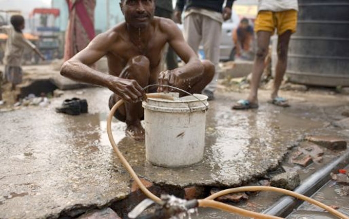 Local Indian residents in a west New Delhi slum use  a broken water pipe to bathe. In a city of 16 million people, one-quarter of New Delhi residents have no access to piped water. (Robert Nickelsberg/Getty Images)