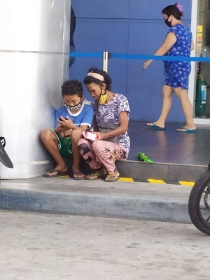 Mother and son sitting with masks half on, looking at phone together