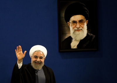 Iranian President Hassan Rouhani waves to journalists next to a portrait of supreme leader Ayatollah Ali Khamenei on June 13, 2015. (Behrouz Mehri/AFP/Getty)