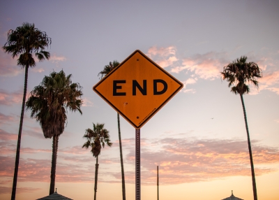 Image of an end of the road sign in front of palm trees.