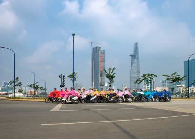 A still from a video set in Ho Chi Minh City that follows twenty-eight scooter riders literally connected by their brightly colored ponchos and identical face masks.