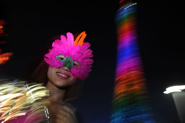 A mask seller stands outside as Caton tower illuminates during a light show rehersal for the opening ceremony for the 16th Asian Games, in Guangzhou on November 10, 2010.