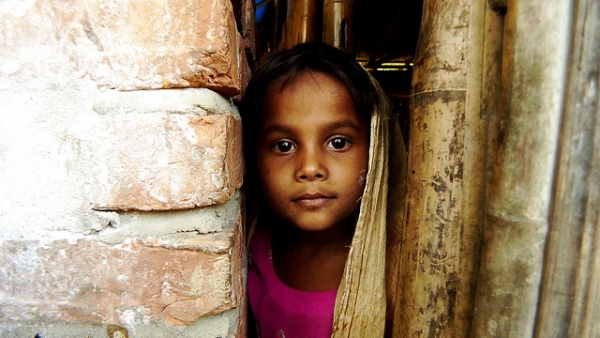 A little girl looks at the camera from behind a brick wall in Teknaf, Bangladesh on November 13, 2012. (No_Direction_Home/Flickr)