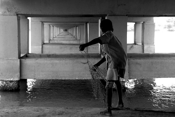 A young boy casts his fishing net into the water beneath a bridge in Chennai, India on May 12, 2013. (Aschevogel/Flickr)