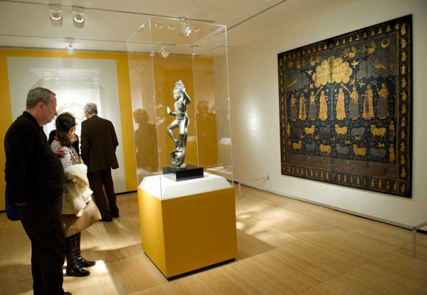 Viewers study a Chola-period bronze sculpture, "Krishna Dancing on Kaliya," in the exhibition "Tales of Wonder: Indian Art from the Asia Society Museum Collection." At right is a 17th-century temple hanging, on first-time view at the museum. (Elena Olivo/Asia Society)