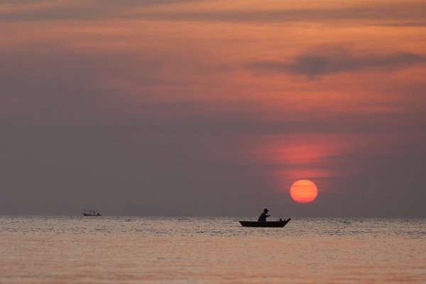 A man in his boat is silhouetted against the setting red sun in Phangan, Thailand on February 18, 2014. (Jens Schott Knudsen/Flickr)