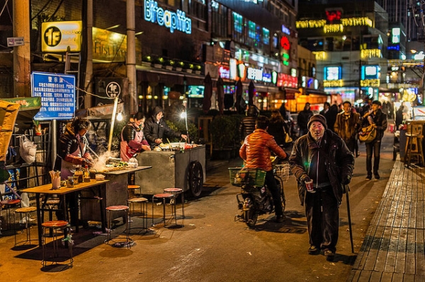 An old man walks along a bustling street at night in Beijing, China on January 12, 2014. (Zhou/Ding/Flickr)