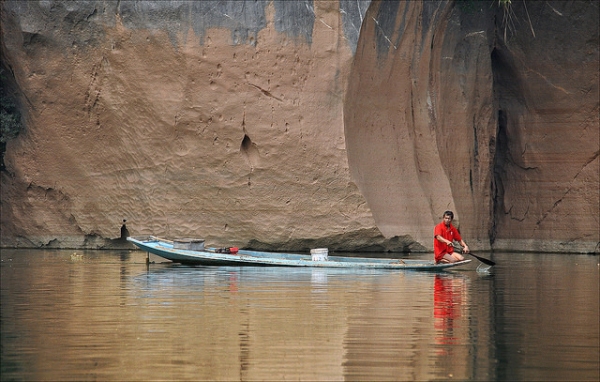 Dressed in bright red, a boatman paddles his way through calm waters in Laos on March 19, 2014. (jean jacques chaffois/Flickr)