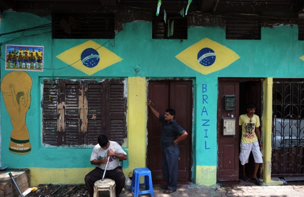 An Indian mechanic (L) sits in front of a house painted with the Brazilian national flag and and an image of the FIFA World Cup in Kolkata on June 15, 2014. (Dibyangshu Sarkar/AFP/Getty Images)
