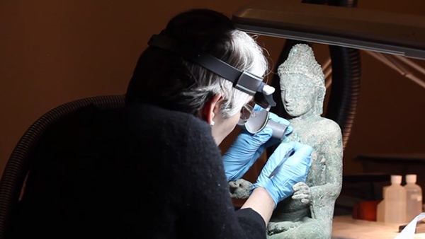 Art conservator Leslie Gat at work removing bronze disease from a sculpture featured in Asia Society Museum's exhibition "Buddhist Art of Myanmar."