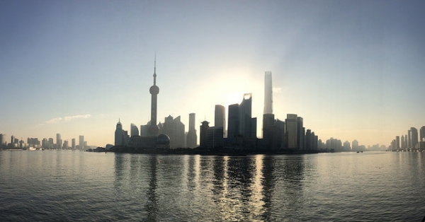 The sun peeks through tall buildings clustered around the water in Shanghai, China on October 3, 2015. (機智的阿卡林醬/ Flickr)