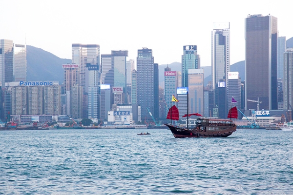 A junk boat with dark, red sails glides past the tall buildings of Hong Kong Island on November 28, 2015. (Tahiat Mahboob)