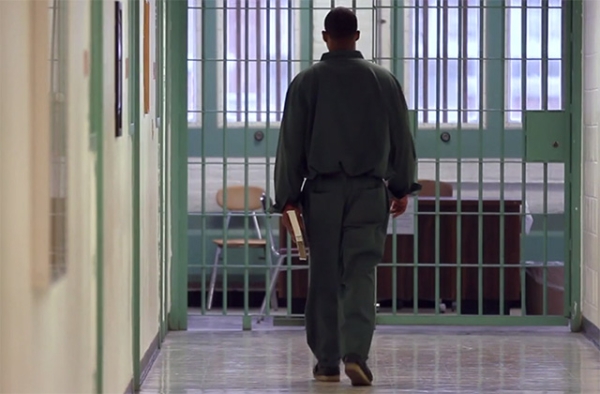 Inmate in New York State carries a book through a prison corridor. (Bard Prison Initiative promotional film screen grab; Winton/duPont Films)