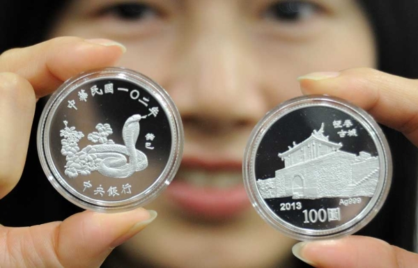 A woman displays two silver coins with designs of a snake (L) and the ancient southern town Hangtsun during a press conference at the Central Bank in Taipei, Taiwan on January 8, 2013. (Sam Yeh/AFP/Getty Images)