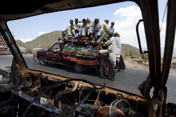 PAKISTAN, JUNE 23 - A car packed with people returning to their villages drives by a burned vehicle left over from the fighting in Pakistan&apos;s Buner district. Over 1.9 million Pakistanis were living in refugee camps as a result of the Pakistani Army&apos;s offensive against the Taliban in tribal areas near the Afghan border. (Paula Bronstein/Getty Images)