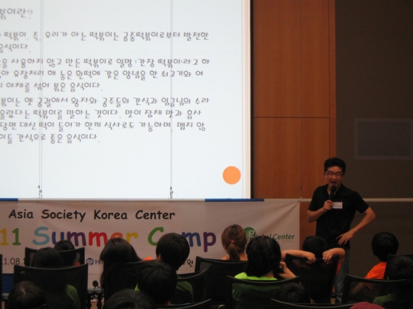 K21 member Sean Kim (with microphone) gives a lecture on the history of Korean food before he begins the cooking class. (Asia Society Korea Center)