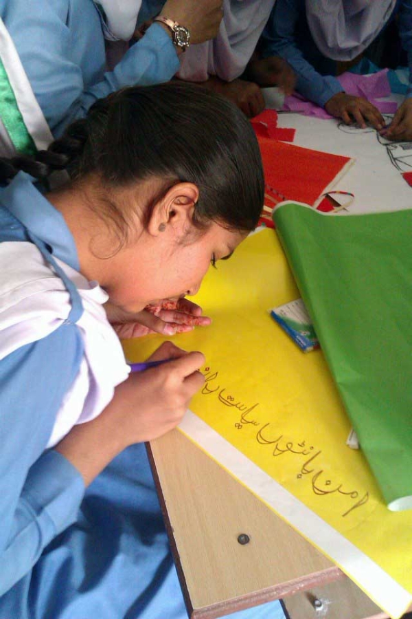 A young student decorates a panel with a slogan during the "Peace-building Thru Artistic Expressions" workshop. (Pakistan Youth Alliance)