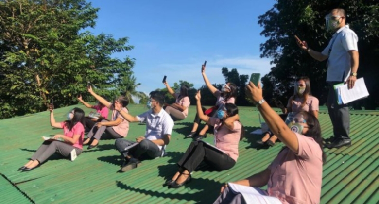 Teachers in uniform on top of rooftop with their hands with phones reaching out
