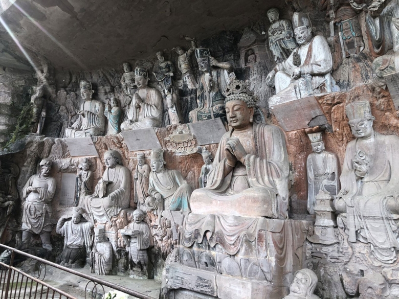 A couple dozen stone figureative sculptures are arranged on on tiers cut into a rock wall. Most appear to be religious in nature