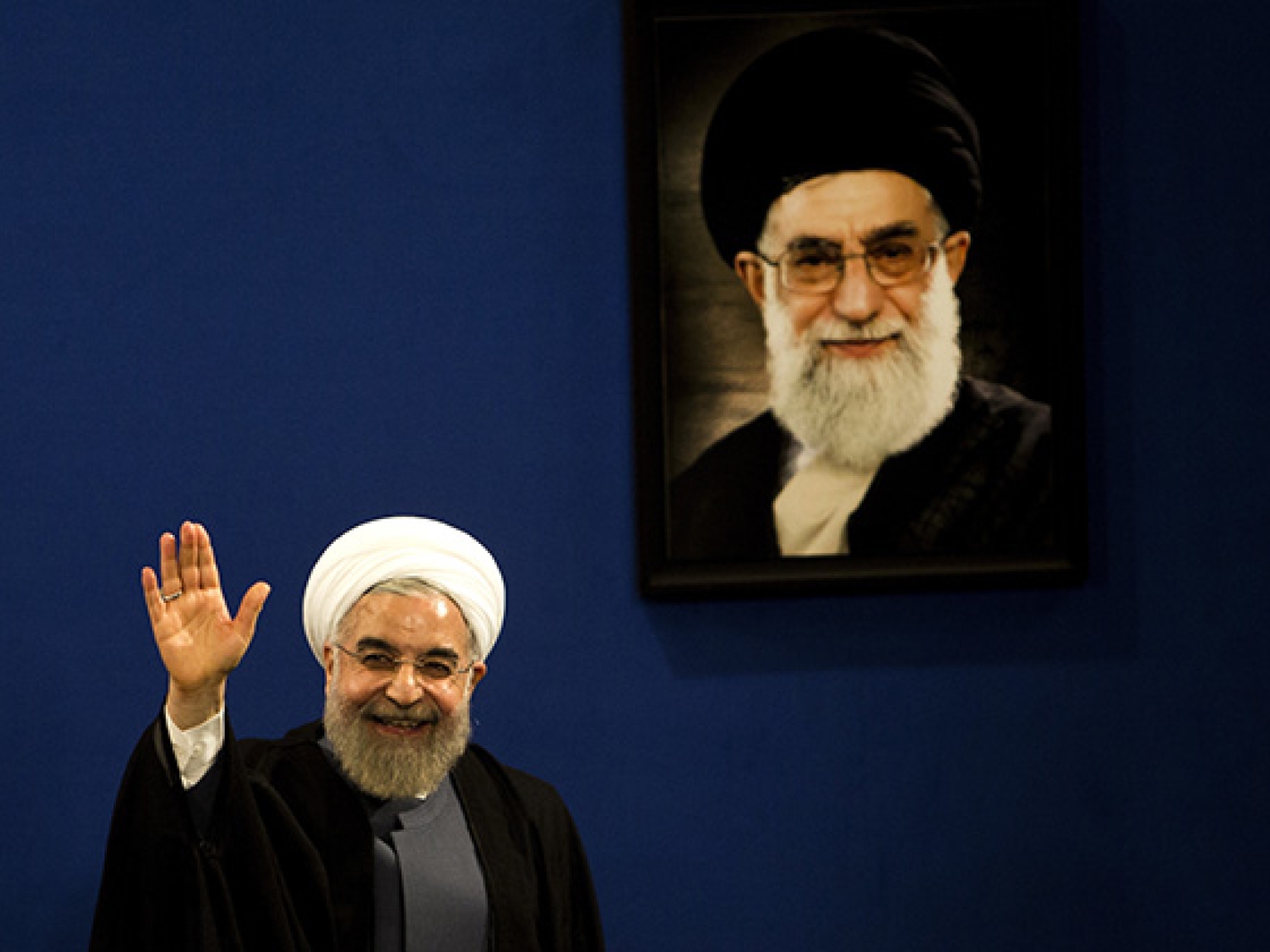 Iranian President Hassan Rouhani waves to journalists next to a portrait of supreme leader Ayatollah Ali Khamenei on June 13, 2015. (Behrouz Mehri/AFP/Getty)