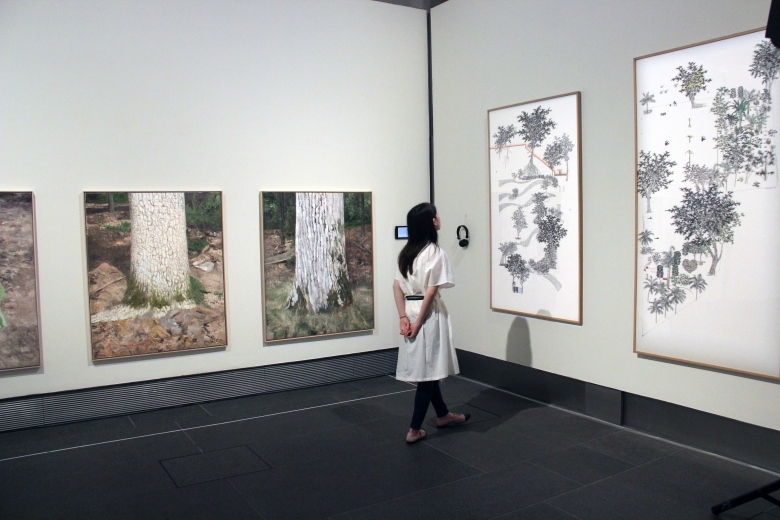 Visitor next to Natee Utarit's paintings of oak tree trunks (left) and looking at Frank Tang's Pocket Park series of paintings (right)