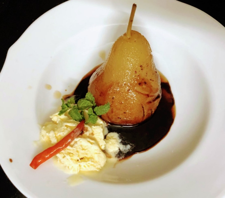 Poached pear dessert with chocolate sauce, vanilla ice cream, and red chili pepper garnish